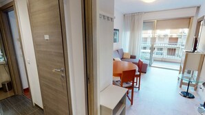 A modern hotel room with a wooden door, a dining area with a table and chairs, a sofa, and a balcony with a view of the city. - Charming 3-Room Apt with Terrace, Near Beach & Parking in Menton (Menton)