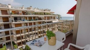 A balcony with a table, chairs, and a magazine. There are multiple floors of buildings in the background, and a palm tree is visible. - Charming 3-Room Apt with Terrace, Near Beach & Parking in Menton (Menton)