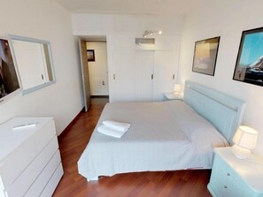 A hotel room with a bed, a dresser, a nightstand, and a door leading to another room.