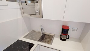 Een praktische kitchenette met een inbouwfornuis, een spoelbak en een koffiezetapparaat.