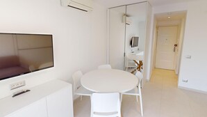 Een moderne, minimalistische kamer met een ronde eettafel, witte stoelen, een flatscreen-tv en een ingebouwde airconditioning.