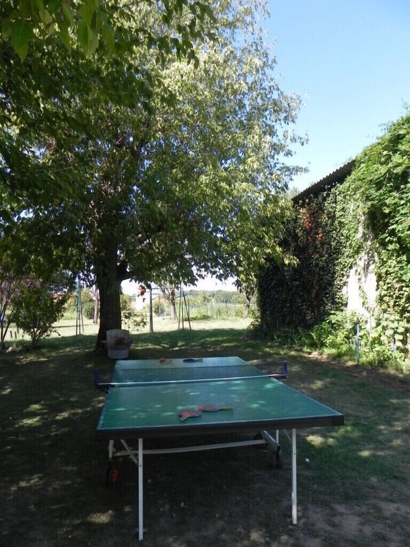 A ping pong table set up outdoors with a tree and a hedge in the background.