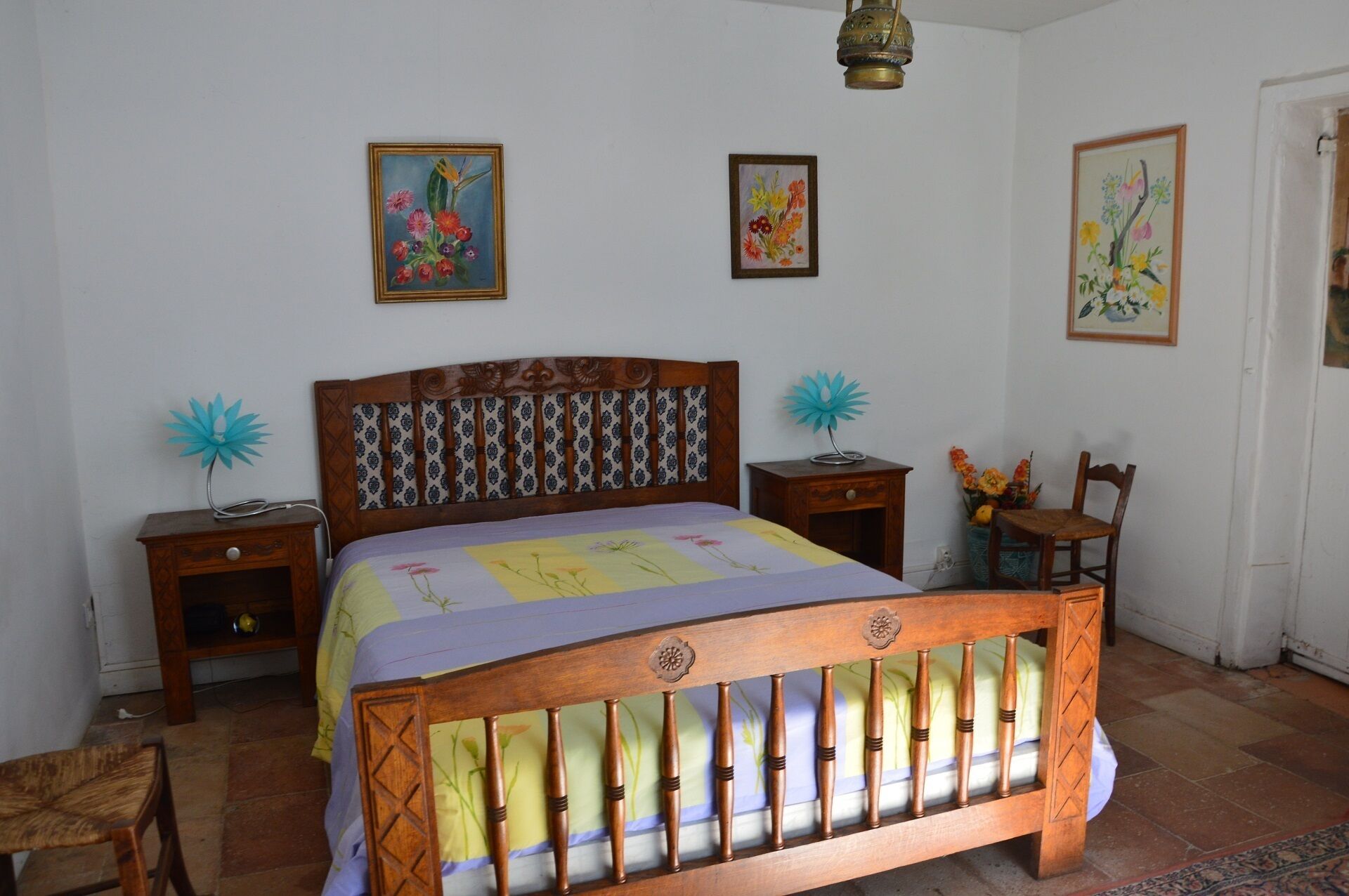 A bedroom with a wooden bed, two bedside tables, a chair, and floral wall art.