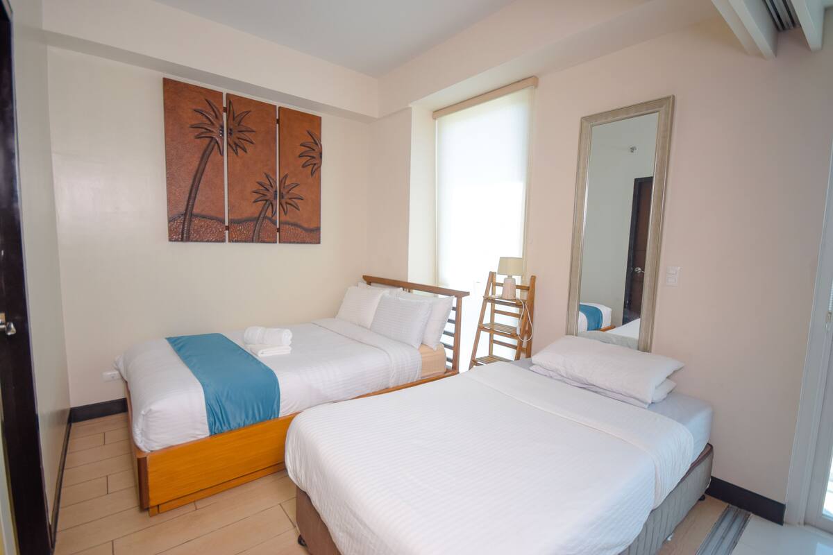 A hotel room with two single beds, a wooden ladder, a large mirror, and a wall art piece.