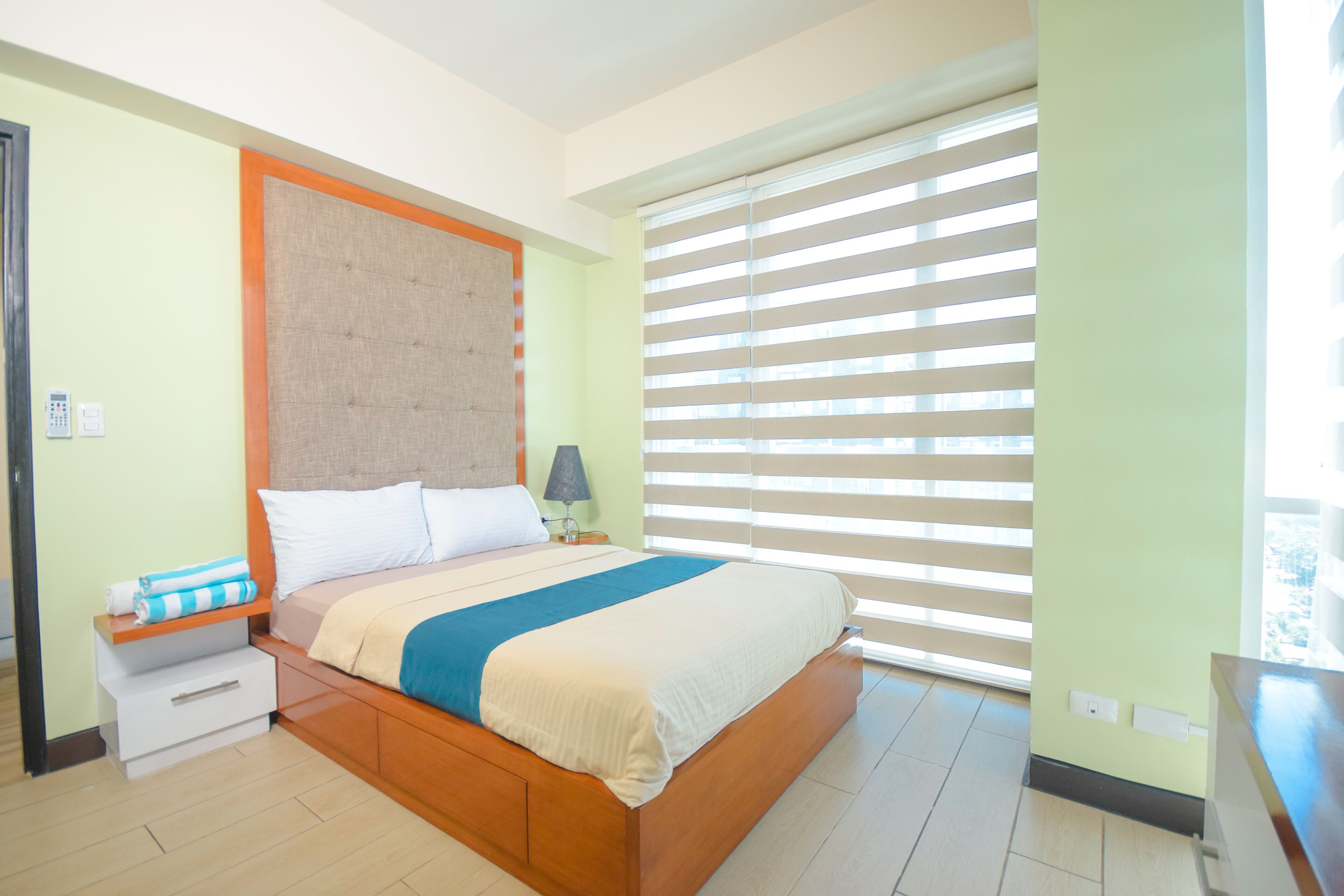 A bedroom with a bed, bedside table, lamp, and a window with blinds.