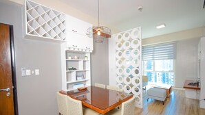 Un comedor moderno con una mesa de madera y sillas de mimbre, una estantería blanca con adornos y una pared con diseño.