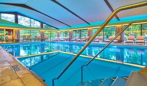 An indoor swimming pool with clear blue water, surrounded by lounge chairs and a glass barrier. - Hotel Das Bayerwald (Lam)