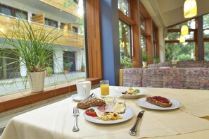 A breakfast setting with a table, plates of food, a cup, and a glass of orange juice. - Hotel Das Bayerwald (Lam)