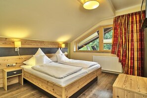 A bedroom with a wooden bed, bedside tables, a window with curtains, and a radiator. - Hotel Das Bayerwald (Lam)