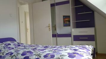 A bedroom with a bed, a wardrobe with a purple accent, and a painting on the wall.