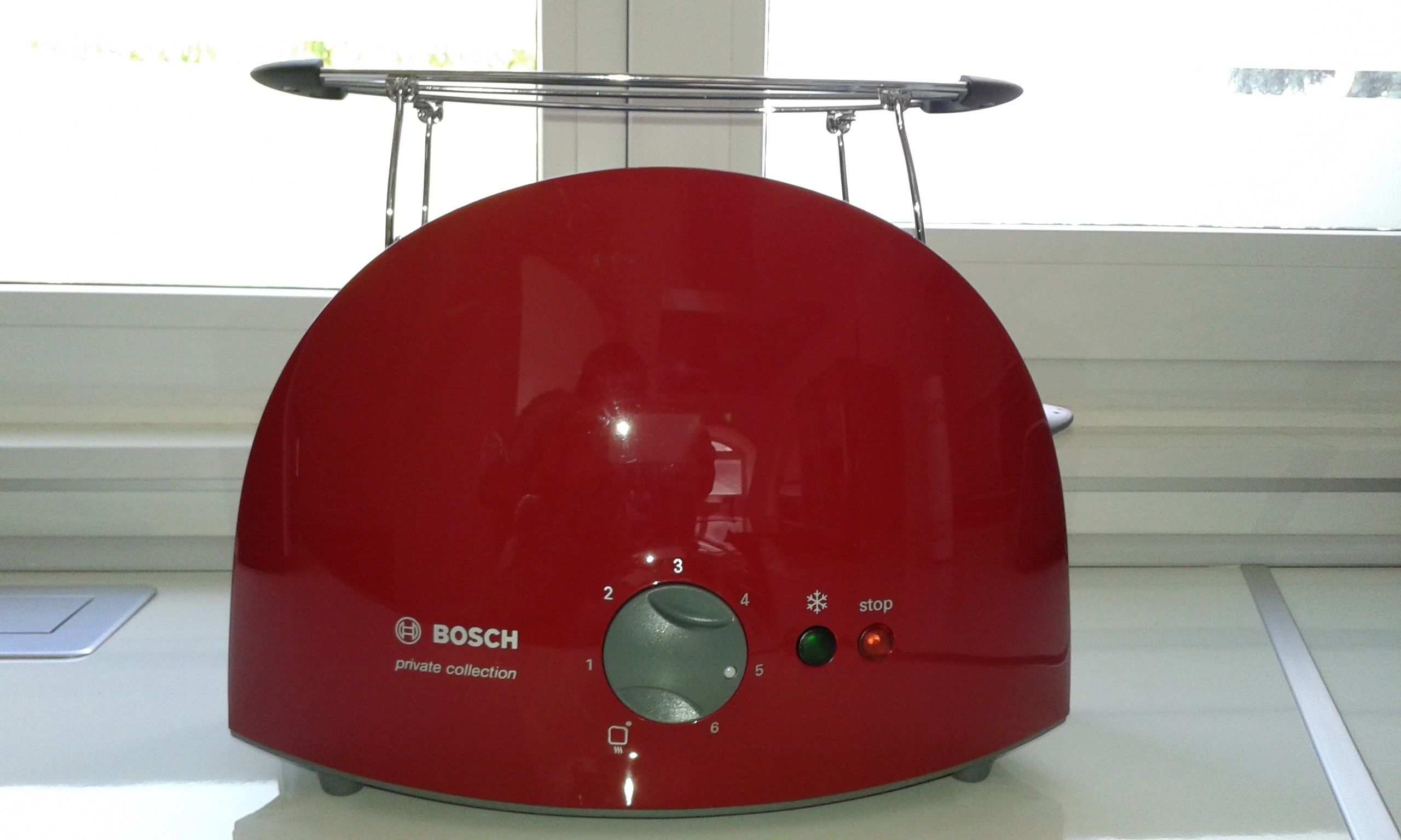Un electrodoméstico rojo Bosch con un panel de control y un asa metálica en la parte superior.