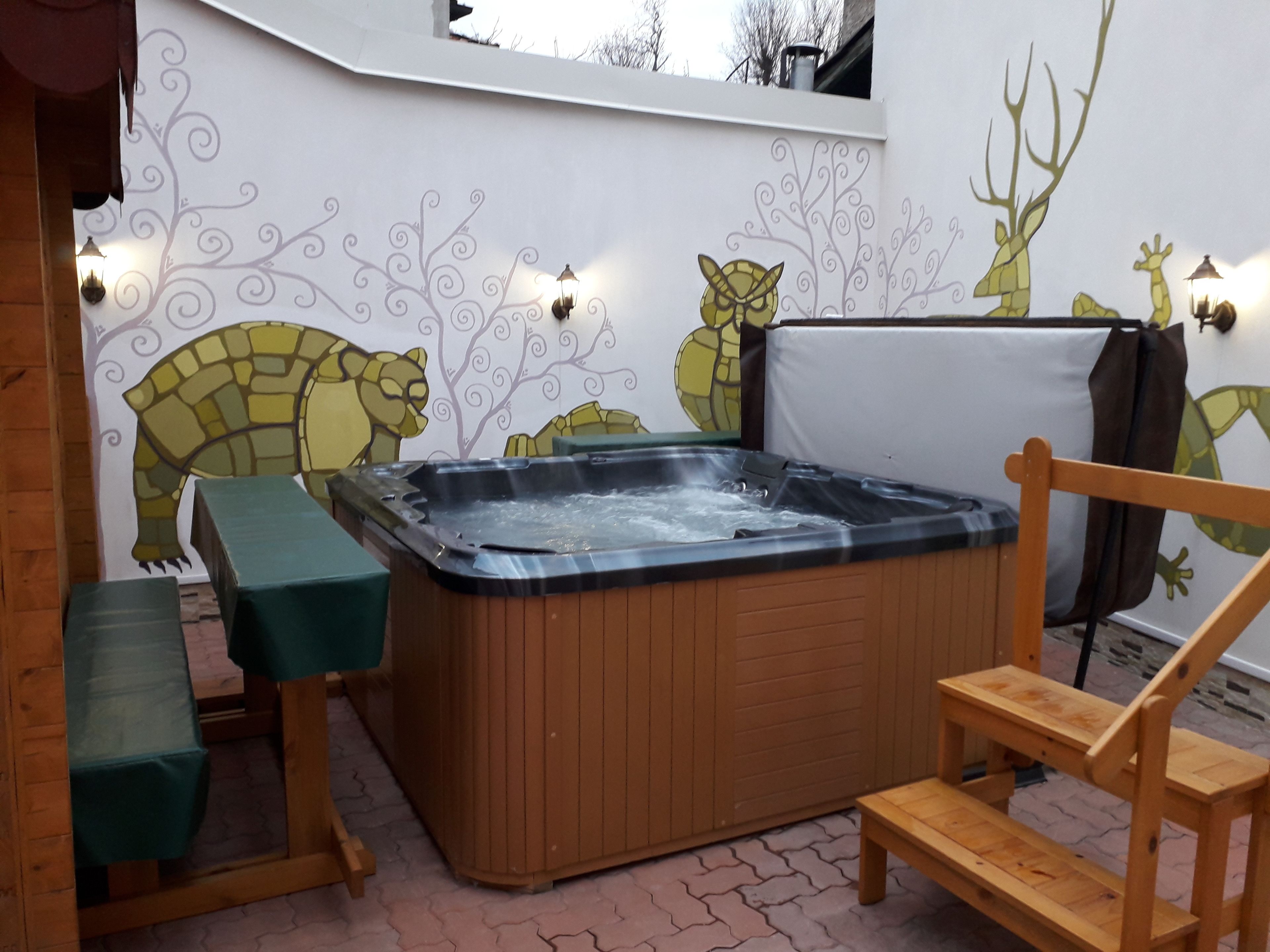 Un jacuzzi con un banco y una silla de madera, rodeado por una pared con murales de animales.