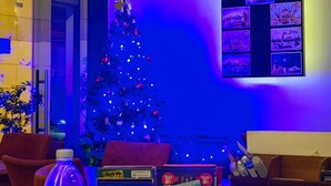Una habitación con un árbol de Navidad, una pared con carteles, un escritorio con una calculadora, una botella y un cubo rojo.