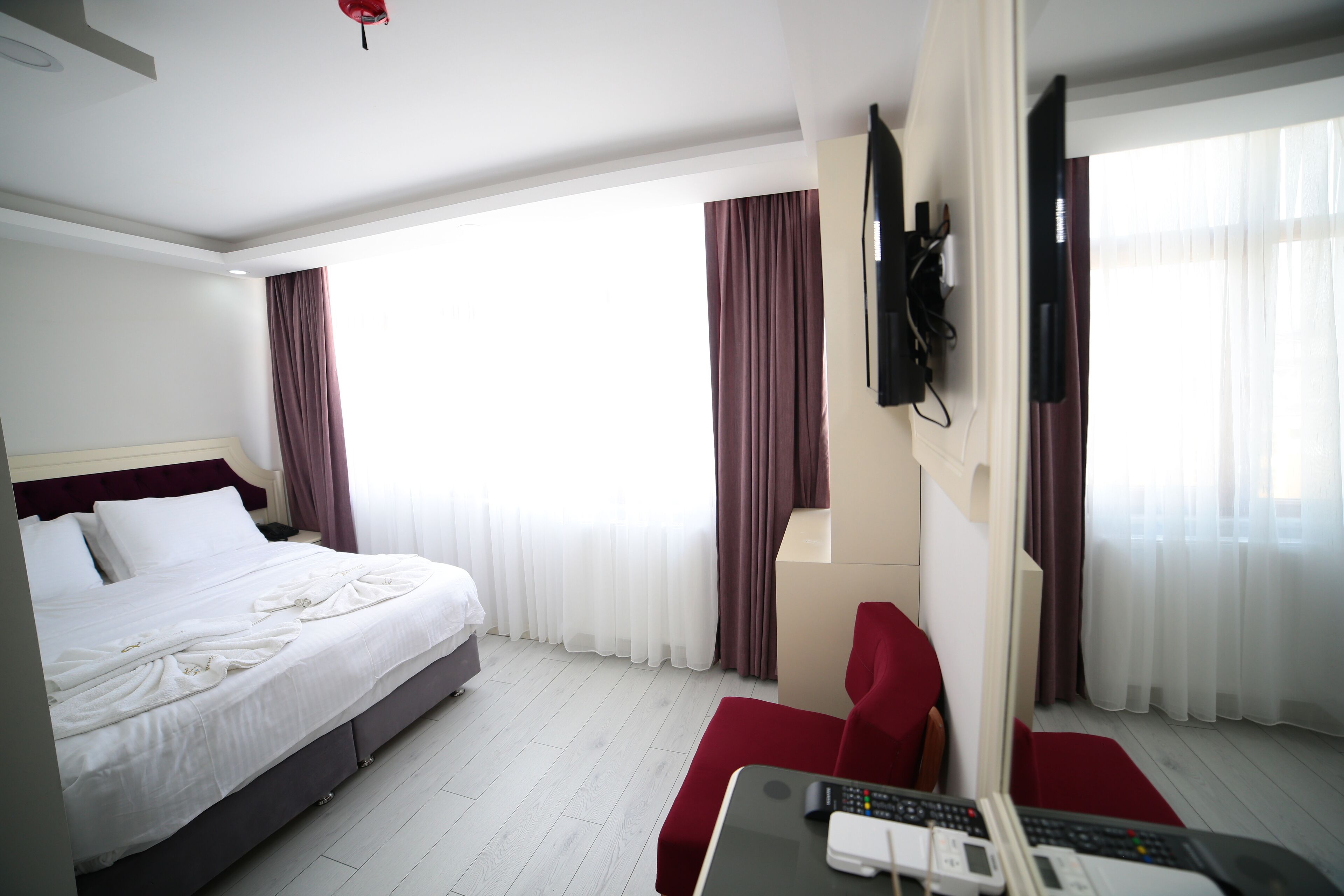 A hotel room with a bed, a desk with a computer and remote, a TV, and curtains.