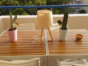 A balcony with a wooden table, two potted cacti, a white chair, and a small candle holder. - Central studio with terrace, air conditioning and parking (Menton)