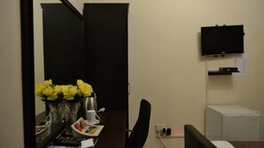 A room with a desk, a television mounted on the wall, a small refrigerator, and a mirror reflecting part of the room. - Jasper Guest House (Selebi-Phikwe)