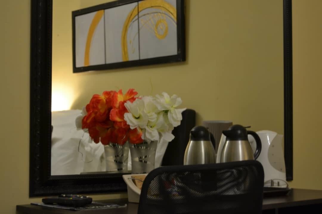 A hotel room with a desk, a vase with flowers, a coffee maker, and a kettle.