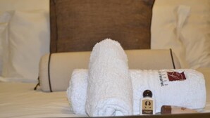 A neatly made bed with a folded white towel and a bottle of lotion. - Jasper Guest House (Selebi-Phikwe)