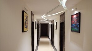 A modern hotel hallway with a polished floor, framed artwork on the walls, and a geometric ceiling design. - The Pacific Hotel, Vadodara (Vadodara)