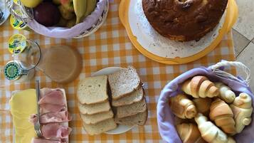 Ein Tisch mit verschiedenen Speisen, darunter Brot, Schinken, Gebäck und Kuchen.