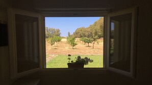 A room with a window overlooking a grassy area with trees and a distant building. - Villa Arzilla Sardegna (Alghero)