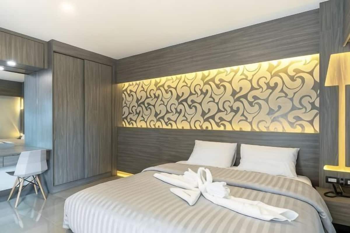 A modern hotel room with a large bed, a desk, and a patterned wall.
