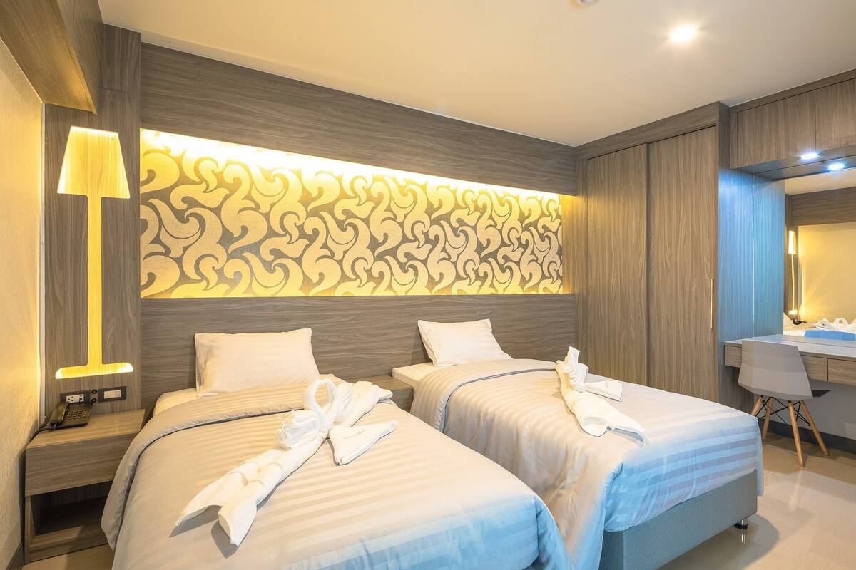 A hotel room with two beds, a bedside lamp, a vanity with a mirror, and a decorative wall panel.
