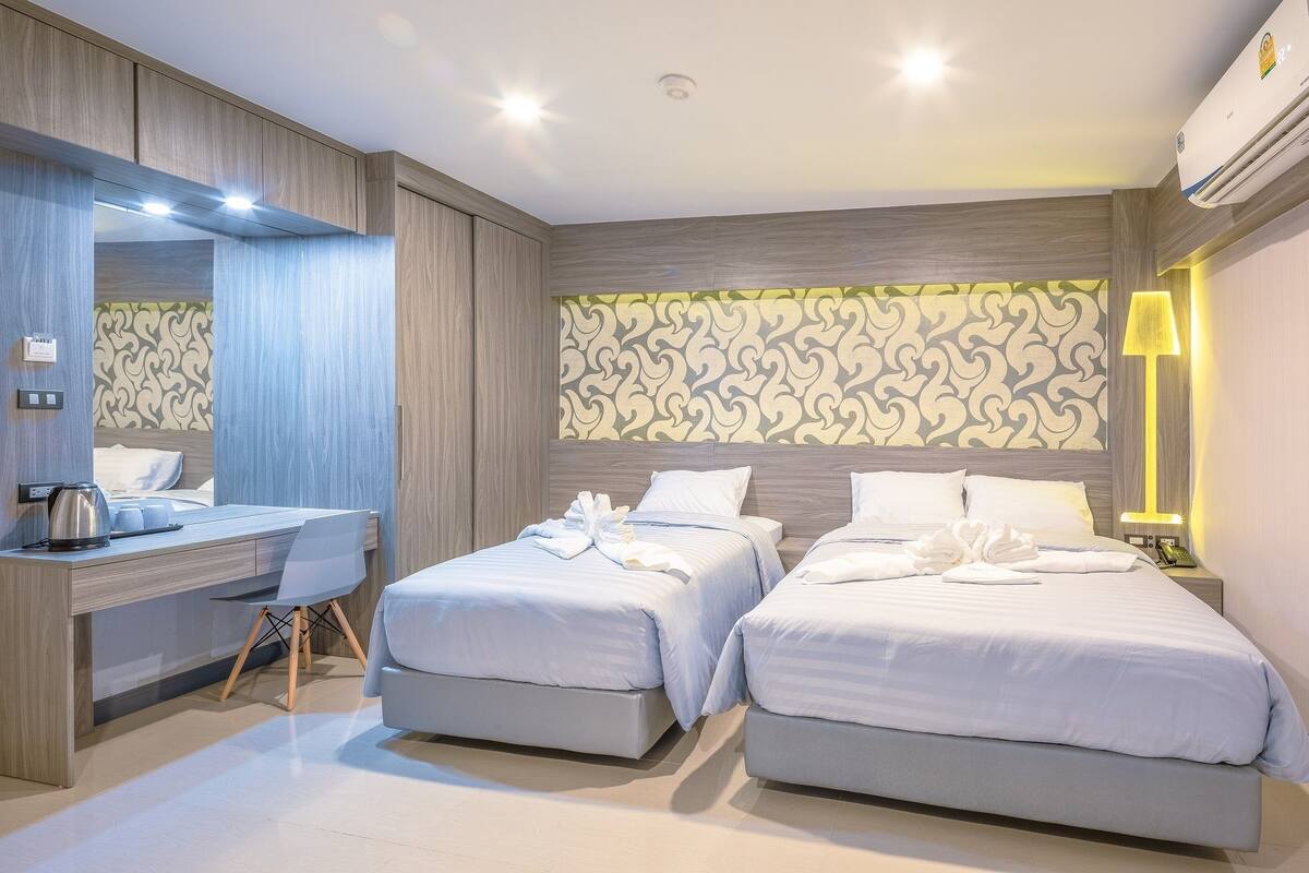 A modern hotel room with two beds, a desk, and a large mirror.