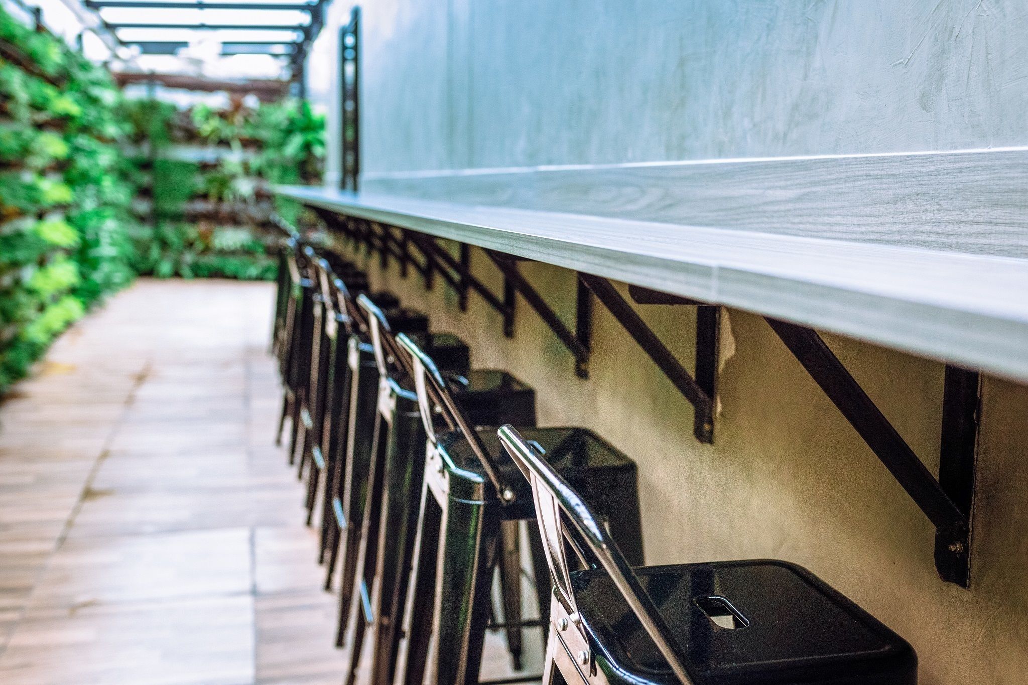 A row of black bar stools with metal legs and black trays, aligned against a wall with a metal railing.