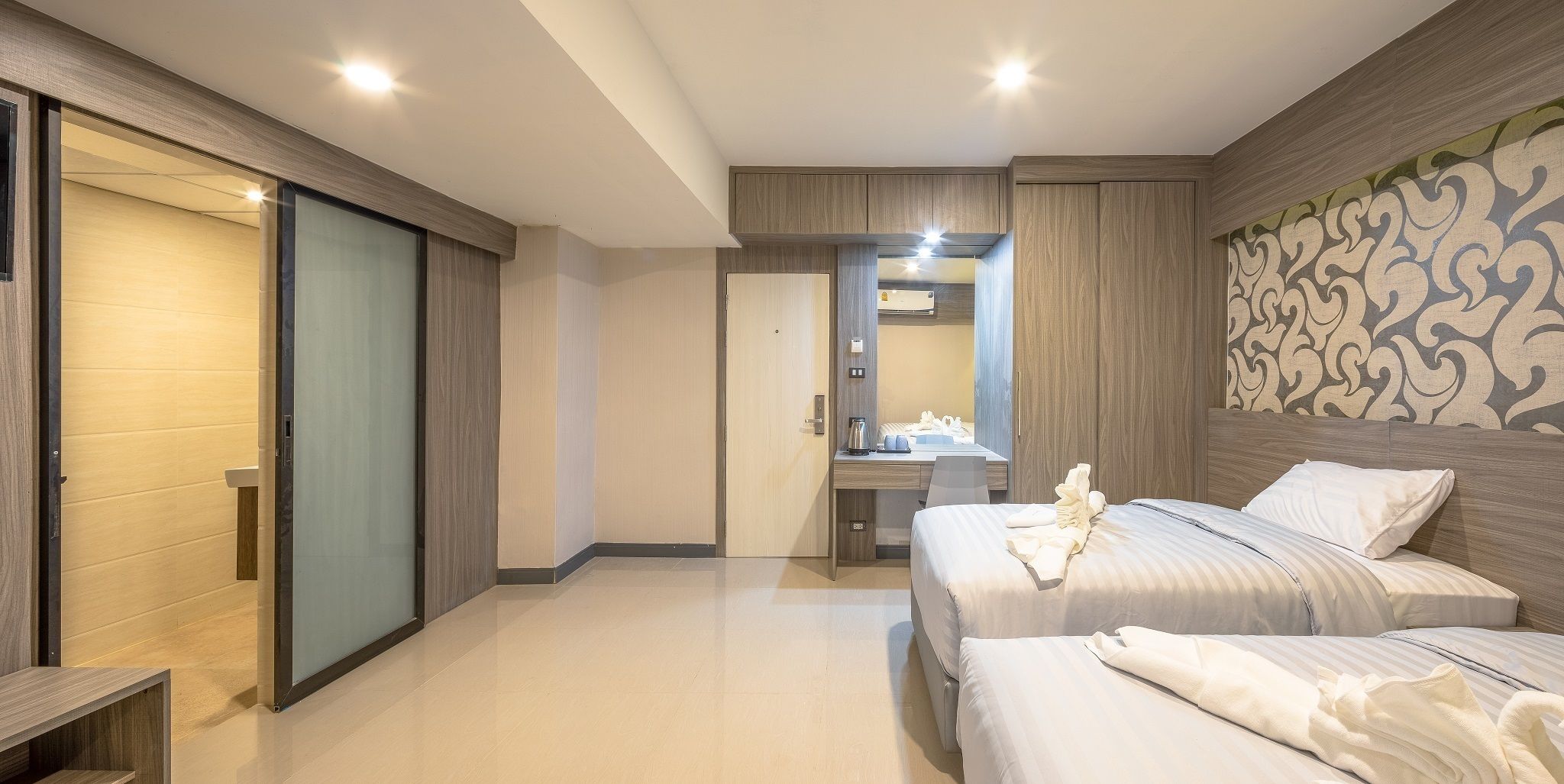 A modern hotel room with two beds, a desk, and a bathroom.
