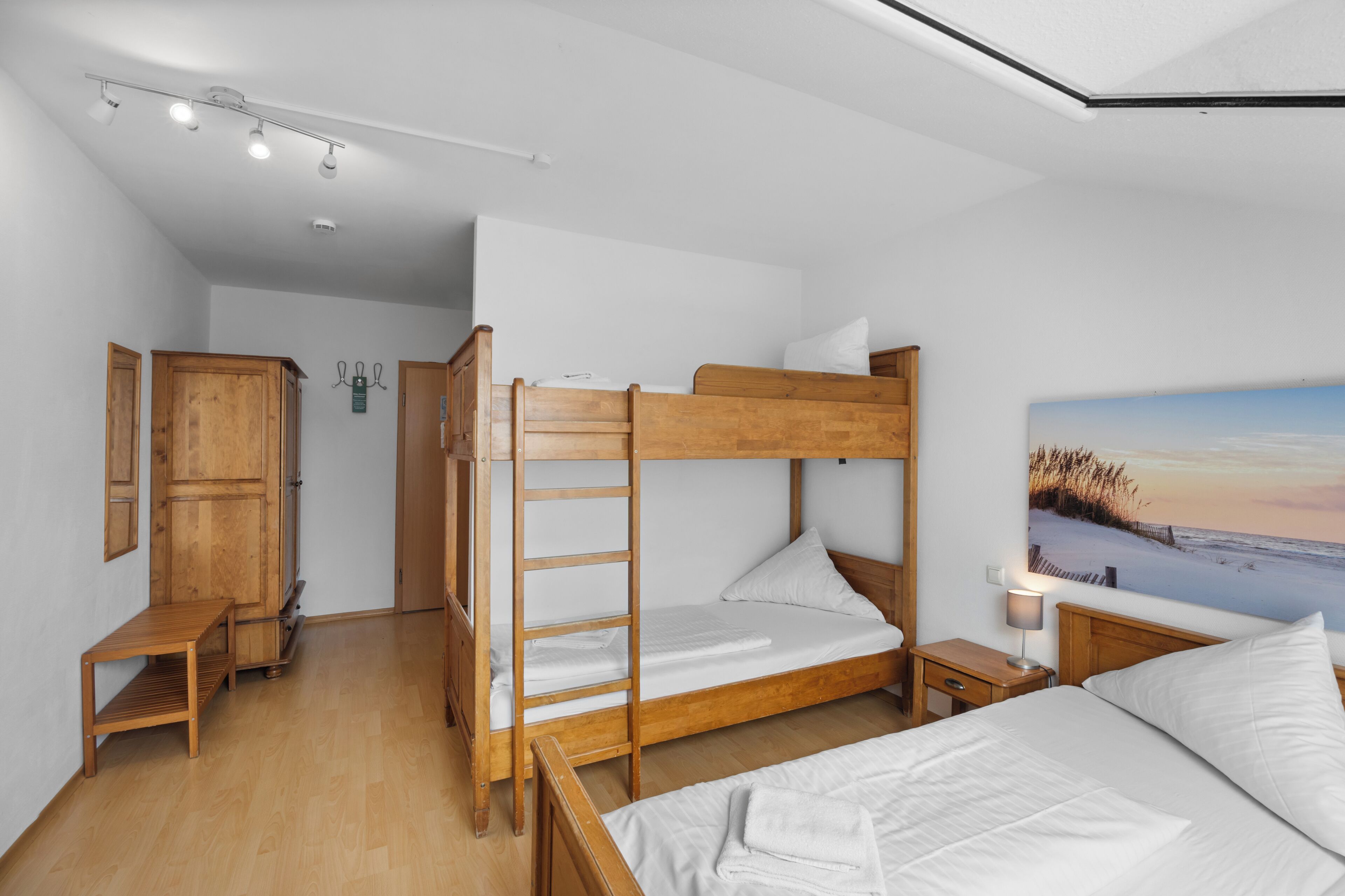 Ein Schlafzimmer mit Etagenbetten, einer hölzernen Bank, einem Nachttisch und einem Bild von einer Strandlandschaft.