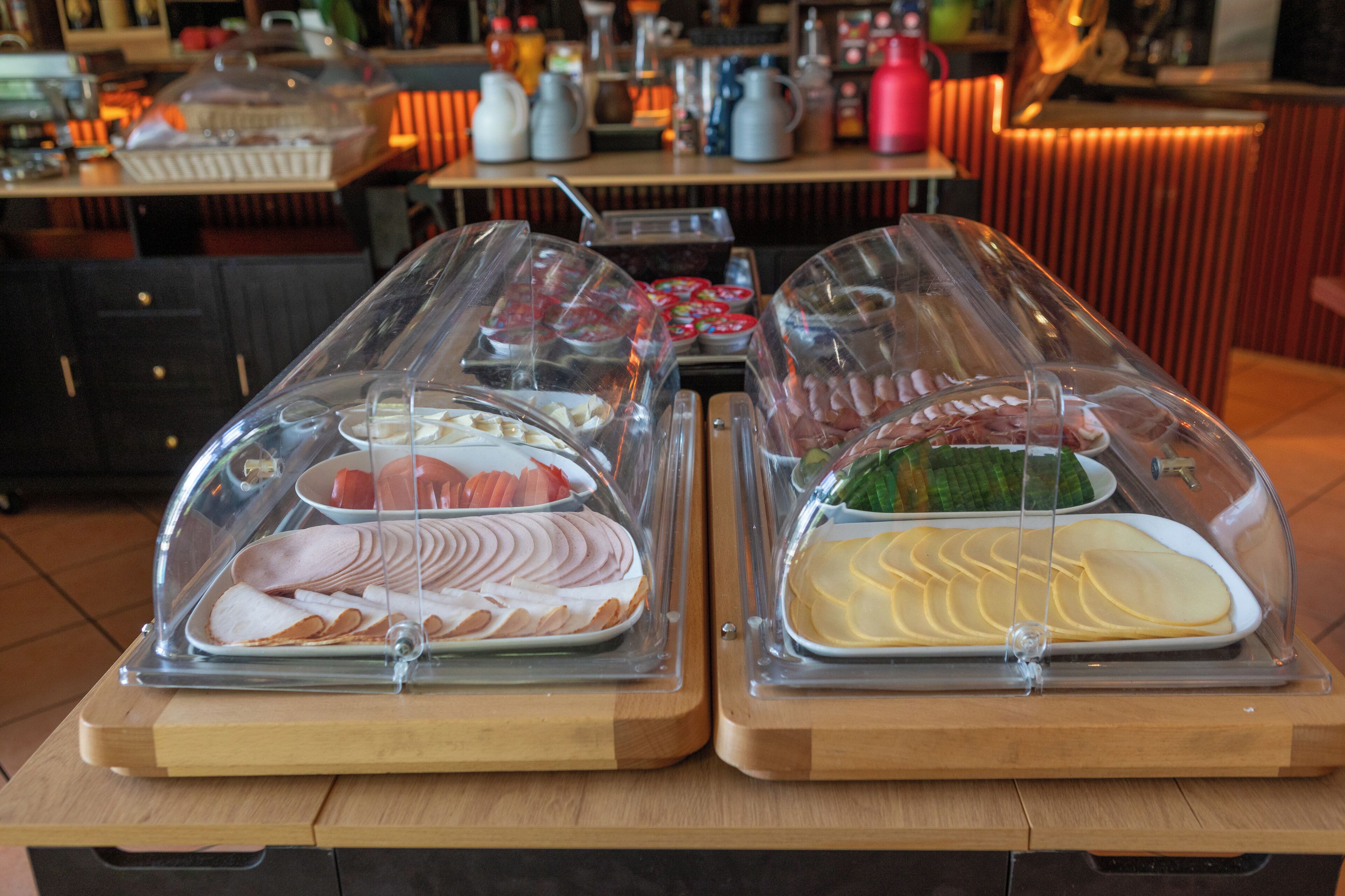 A buffet with various food items covered in plastic domes, a coffee machine, and a kettle on the counter.