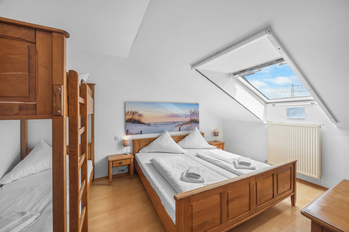 Une chambre avec un lit superposé, un lit simple, une lucarne, un tableau, une table de chevet et un radiateur.