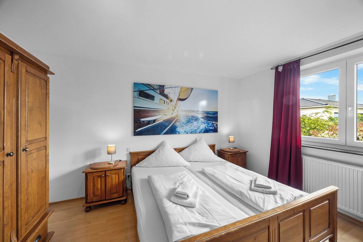 Une chambre à coucher avec un lit, une armoire en bois, des tables de chevet et une fenêtre avec des rideaux.