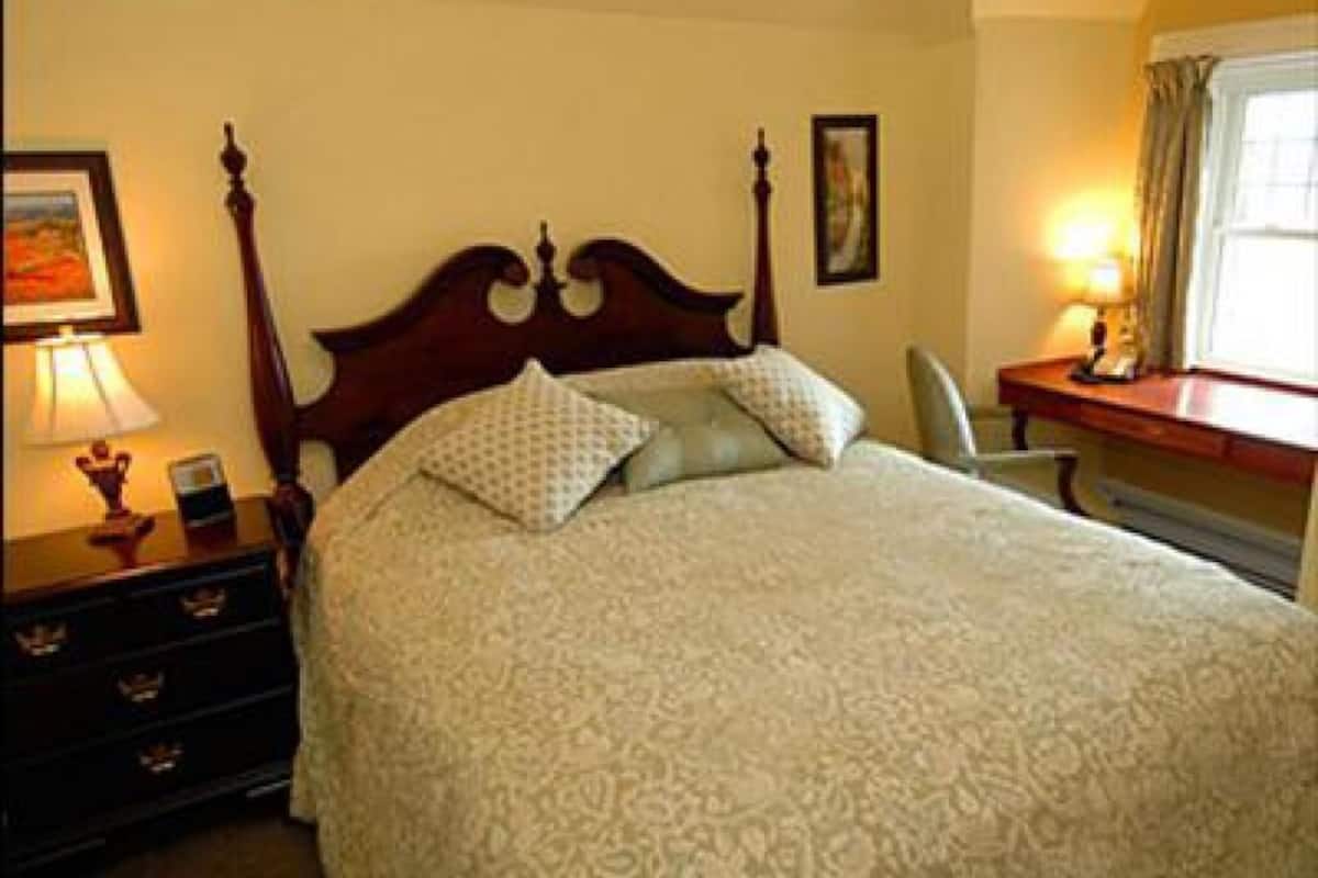 A neatly made bed with a patterned bedspread, a wooden headboard, and a bedside table with a lamp.