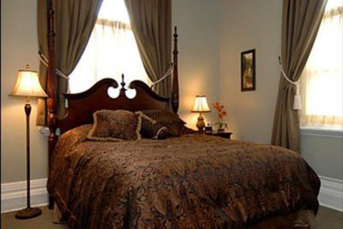 A bedroom with a large bed, two bedside lamps, and curtains on the windows.