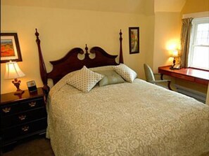 A neatly made bed with a wooden headboard, a bedside table with a lamp, and a window with curtains.
