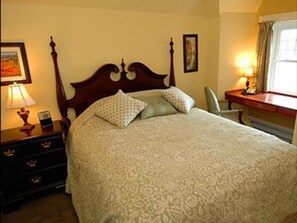 A neatly made bed with a patterned bedspread, a bedside table with a lamp, and a chair by a window.