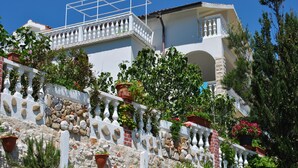 Un bâtiment à la façade blanche, doté d’un socle en pierre et d’une balustrade blanche. Des plantes et des fleurs en pot sont disposées sur la balustrade.
