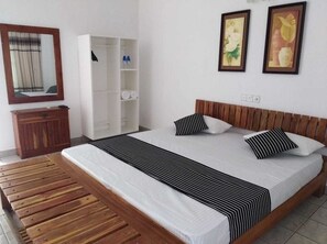Un dormitorio con cama de madera, ropa de cama blanca, un banco de madera, un armario y dos cuadros en la pared.