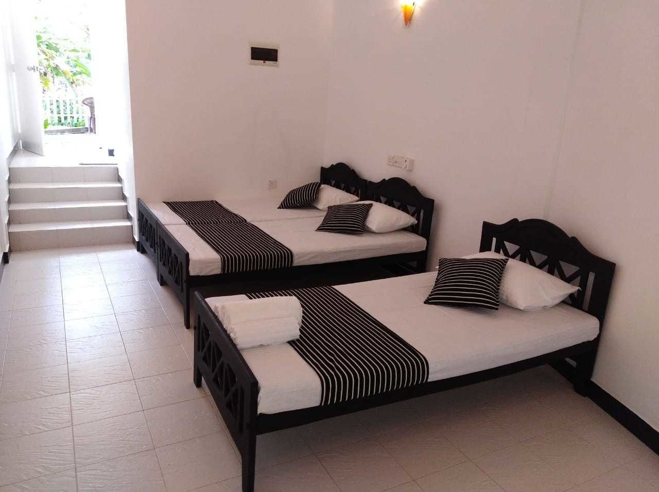 A hotel room with three single beds arranged in a row, a staircase leading to an outdoor area, and a wall-mounted light fixture.