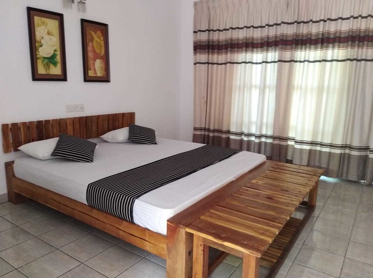Uma cama com cabeceira de madeira, um banco e duas molduras na parede.