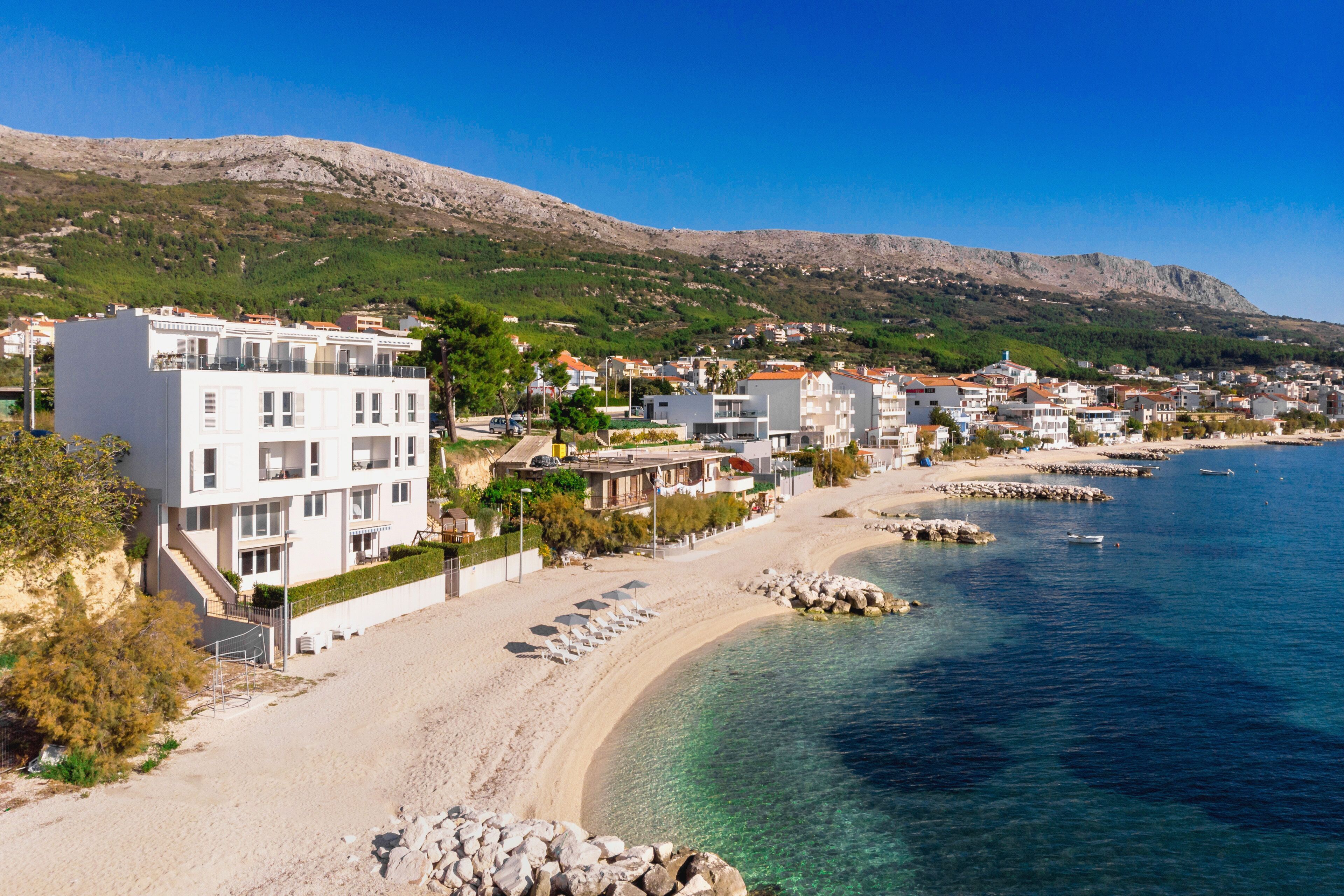 A coastal town with a sandy beach, clear blue waters, and a mountainous backdrop.
