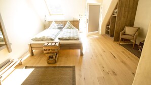 A bedroom with a wooden bed, a small wooden chest, a chair, and a staircase leading to a loft area. - Hotel Kolonieschänke (Burg (Spreewald))