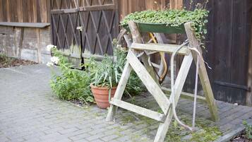 A wooden easel with a green planter on top, positioned on a brick pavement next to a wooden fence and a potted plant.