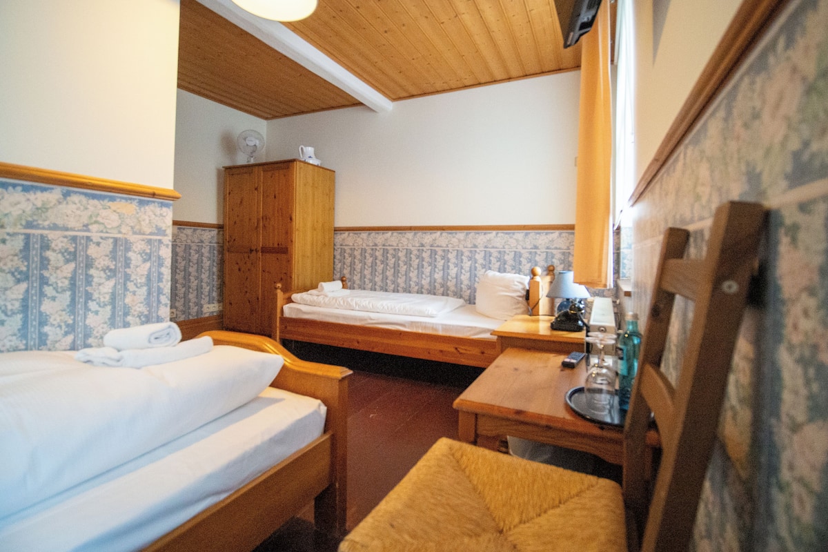 Une petite chambre agréable, dotée de deux lits simples, d’une armoire en bois, d’une petite table avec une lampe et d’une chaise.