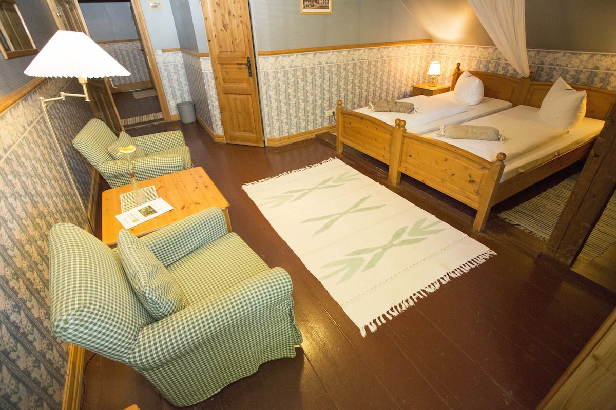 Une chambre avec deux lits simples, une table en bois, un canapé à carreaux verts et un tapis à motifs.