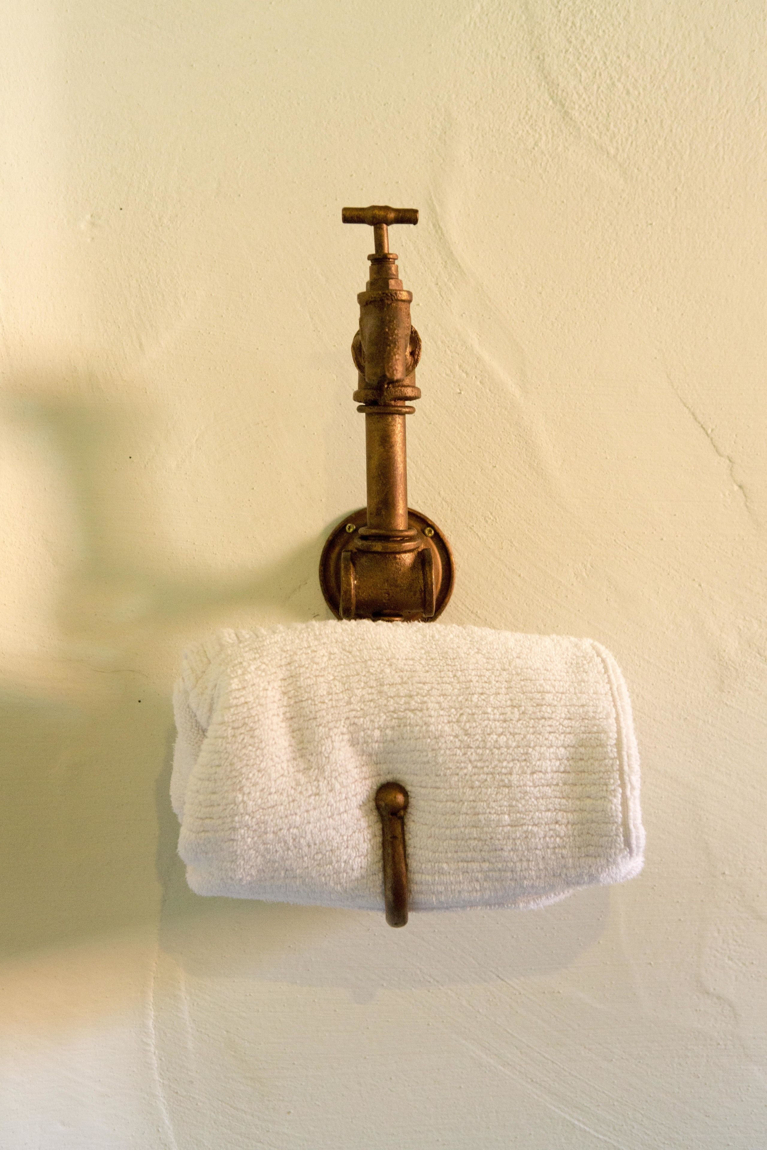 A bathroom with a white towel hanging on a towel rack, a brass faucet, and a plain wall.