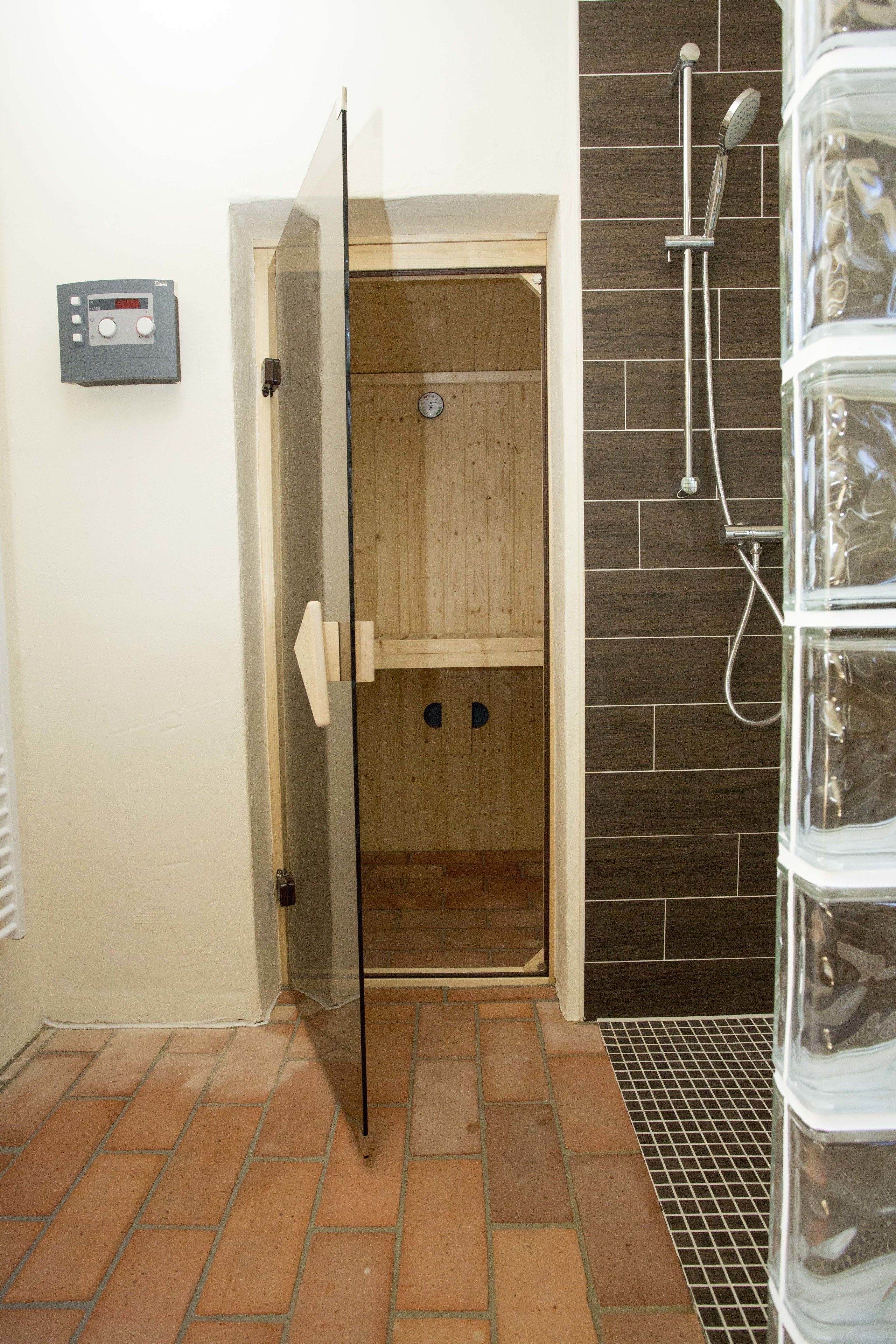 Un sauna avec une porte en bois, un panneau de commande et un espace douche doté d’un mur carrelé.