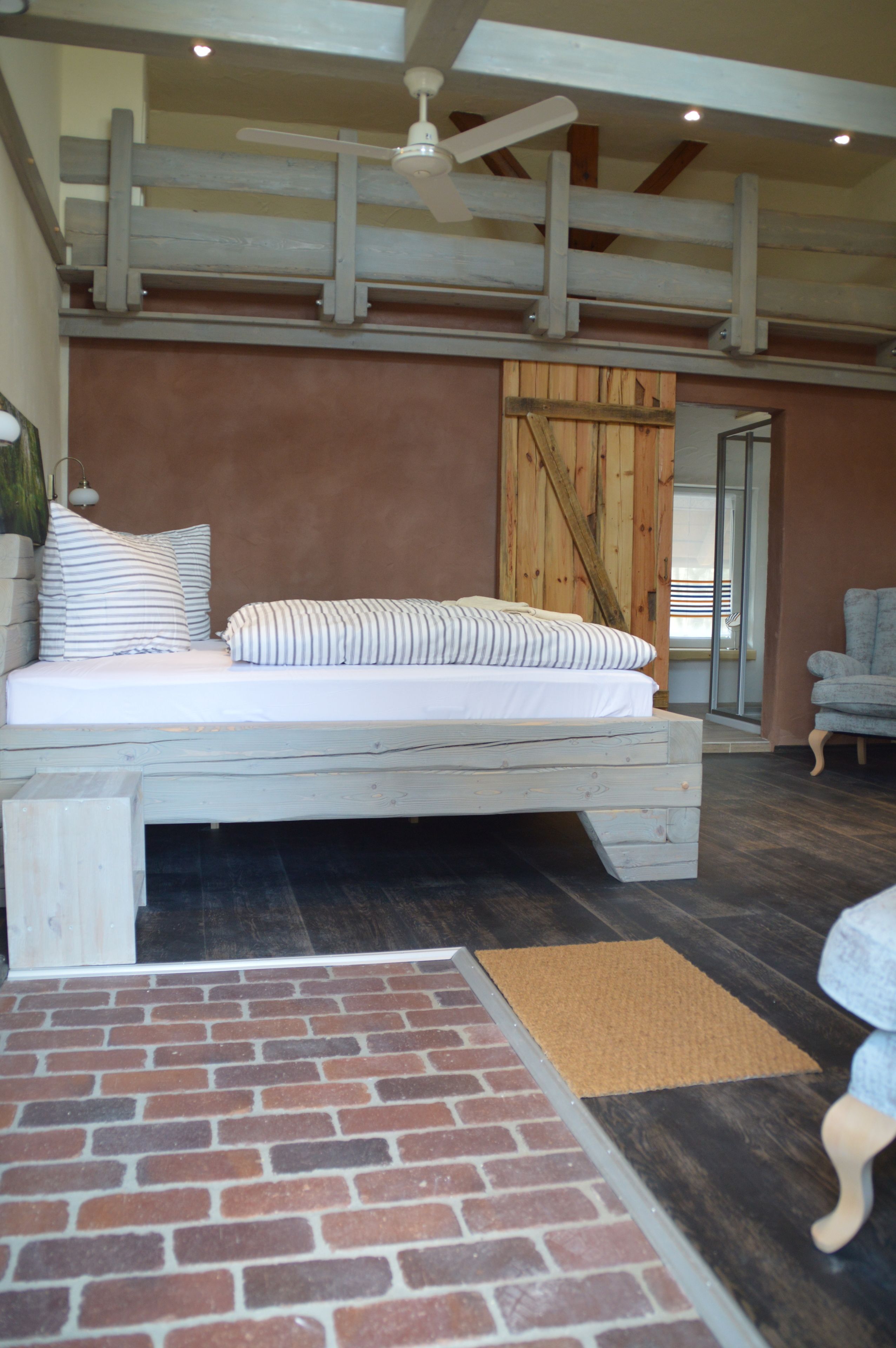 A bedroom with a wooden bed, a brick-patterned rug, and a ceiling fan.